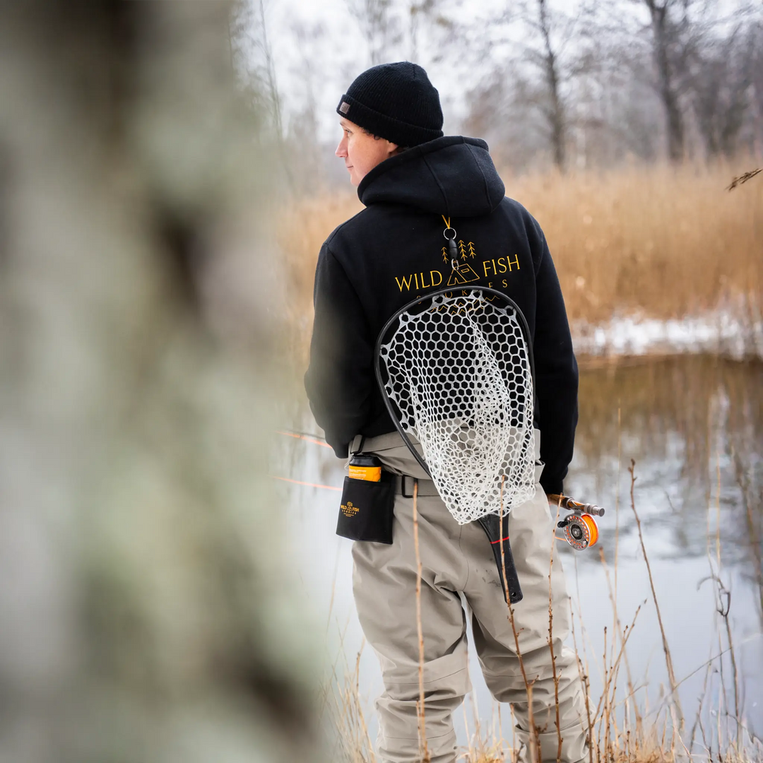 Bluza wędkarska Wild Fish Stories z dużym logo na plecach noszona podczas łowienia muchowego nad wodą, outdoorowy styl życia