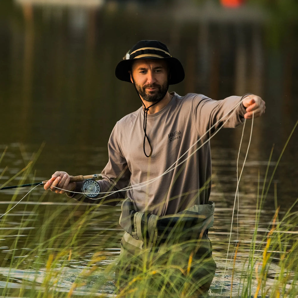 Longsleeve Wild Fish Stories Camper Chill podczas łowienia muchowego w wodzie, mężczyzna w kapeluszu, outdoorowy longsleeve z logo na piersi, styl kamper i slow fishing