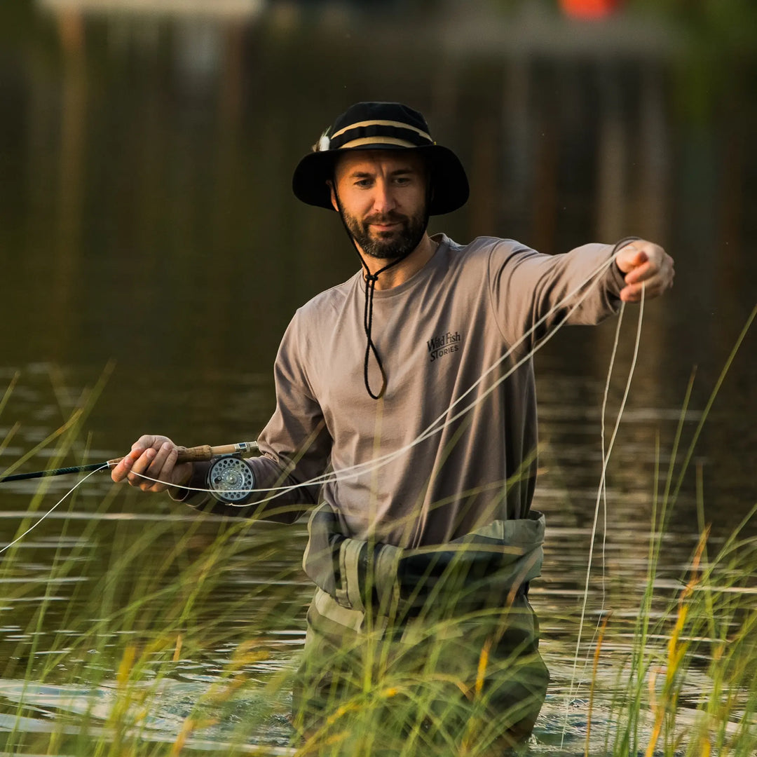 Longsleeve Wild Fish Stories Camper Chill podczas łowienia muchowego w wodzie, mężczyzna w kapeluszu, outdoorowy longsleeve z logo na piersi, styl kamper i slow fishing