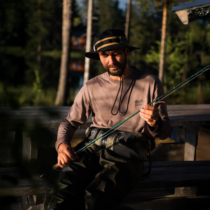 Longsleeve Wild Fish Stories Camper Chill noszony nad wodą, mężczyzna przygotowujący wędkę, outdoorowy longsleeve z logo na piersi, klimat kamper, slow fishing i wypoczynek w naturze