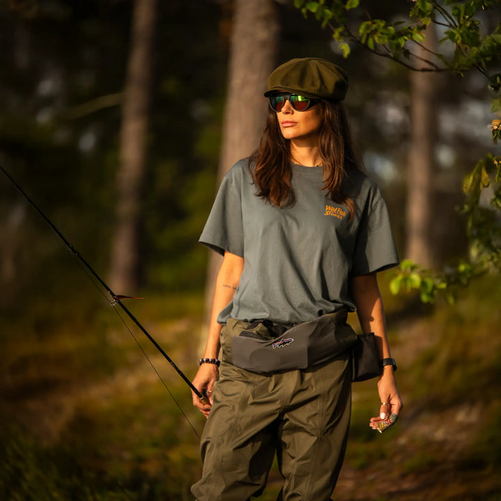 Koszulka Wild Fish Stories noszona przez kobietę podczas wędkowania w lesie, outdoorowy styl życia, odzież wędkarska premium