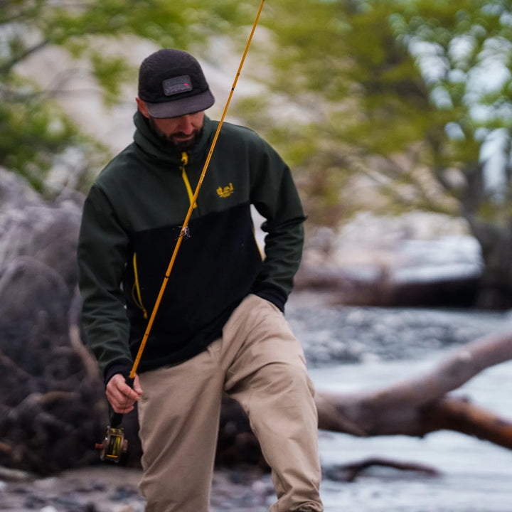 Angler in Wild Fish Stories dark green and black hoodie wading through a rocky river with a fly rod and reel