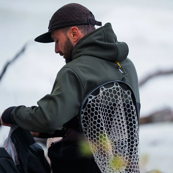 Back view of angler wearing Wild Fish Stories olive hoodie with a landing net clipped to the back, preparing gear outdoors